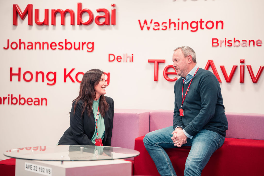 Two Virgin Atlantic employees talking on a red sofa